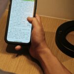 A person holding a smartphone, reading content indoors with focused light.