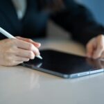 Close-up of a woman using a stylus with a tablet in a modern workspace.