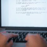 A close-up shot of hands typing a film script on a laptop, focusing on creativity and screenplay writing.