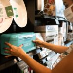 A woman shopping for a turquoise bread bin in a store while wearing a face mask.